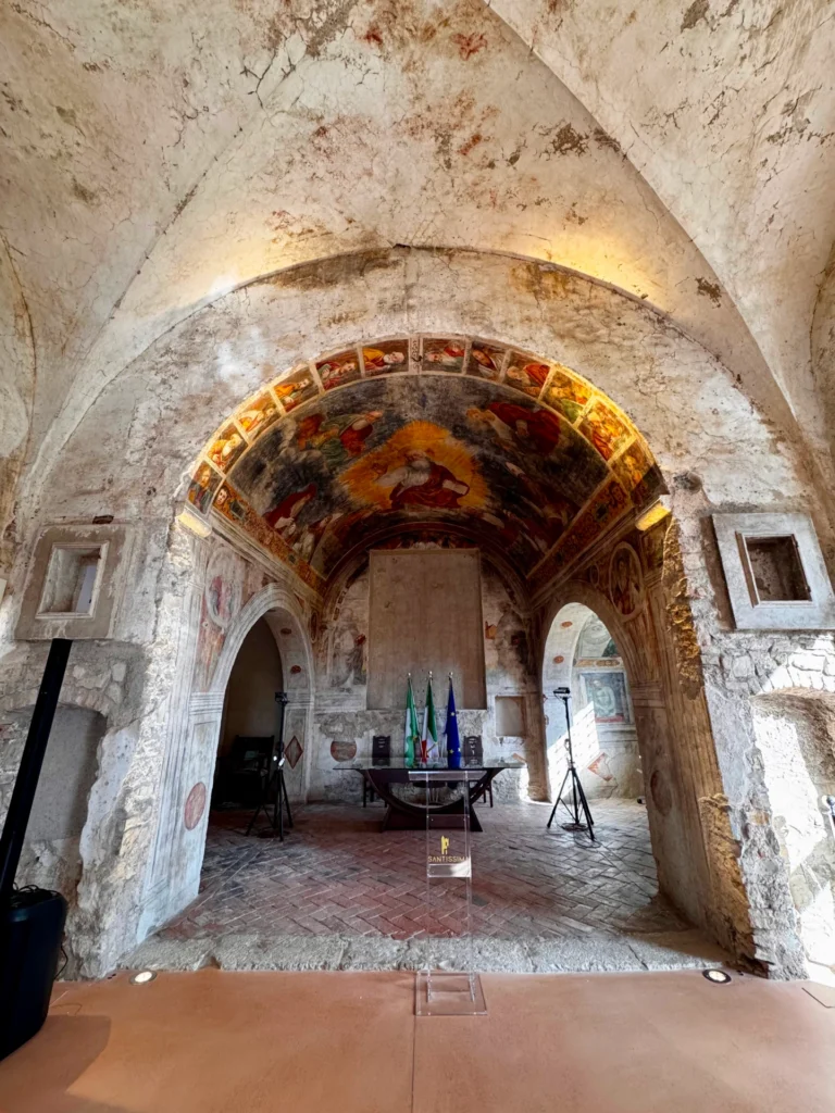 affresco-abside-santissima-gussago-interni Interno della Santissima di Gussago con affresco rinascimentale nell'abside raffigurante Dio Padre e figure sacre tra archi in pietra.