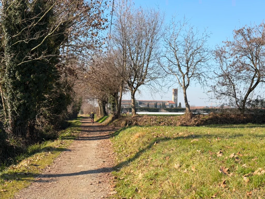 Ciclista lungo il percorso nero Extra Brut con vista sull'Abbazia di San Nicola a Rodengo Saiano, Franciacorta.