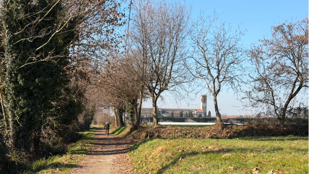 Ciclista sul sentiero sterrato del Percorso Nero Franciacorta verso l'Abbazia di San Nicola a Rodengo Saiano.