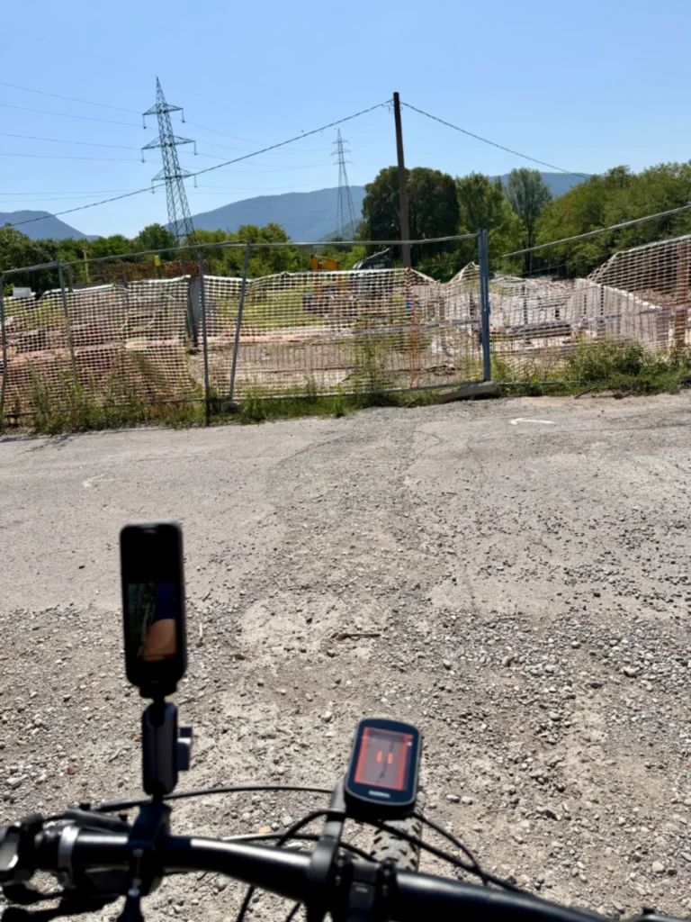 Manubrio di una mountainbike con ciclocomputer e videocamera di fronte a una recinzione di cantiere che sbarra la strada a Concesio