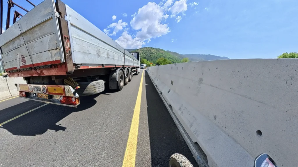 Vista dal manubrio di una bicicletta stretta tra un grande camion rimorchio e una barriera New Jersey in cemento sulla Strada Provinciale 19 a Concesio
